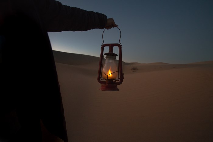 Person holding a lantern in the desert at dusk