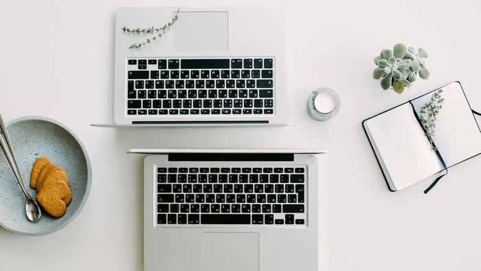 Two MacBooks, Cookies, Candle, and Notebook on White Desk