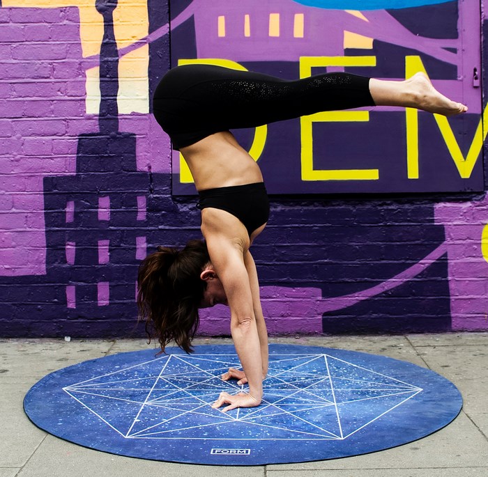 Woman performing a handstand on a round mat with graffiti background