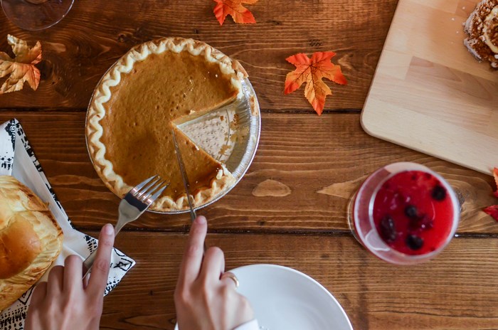 Hands cutting a pumpkin pie on a wooden table