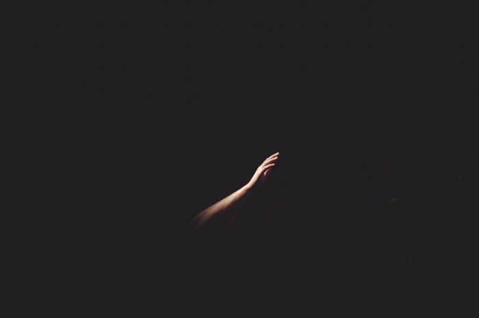 A Caucasian arm reaches out of darkness