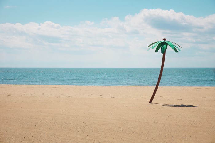 Fake palm tree on a sandy beach with ocean and clouds