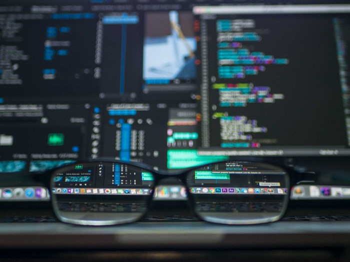 Glasses reflecting computer screen with code and video editing software