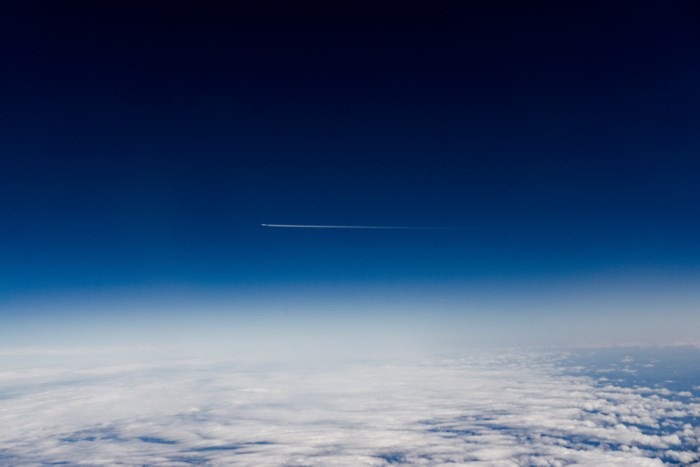 Airplane contrail in a clear blue sky above clouds
