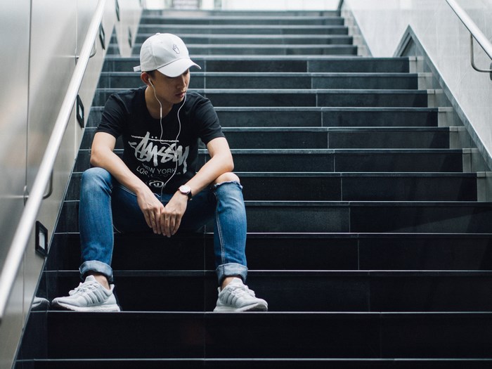 Man wearing a Stussy t-shirt and ripped jeans sitting on stairs