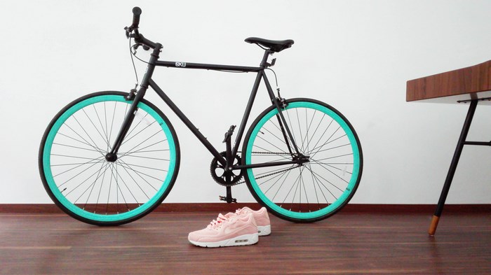Black fixed wheel bicycle with teal rims and pink sneakers