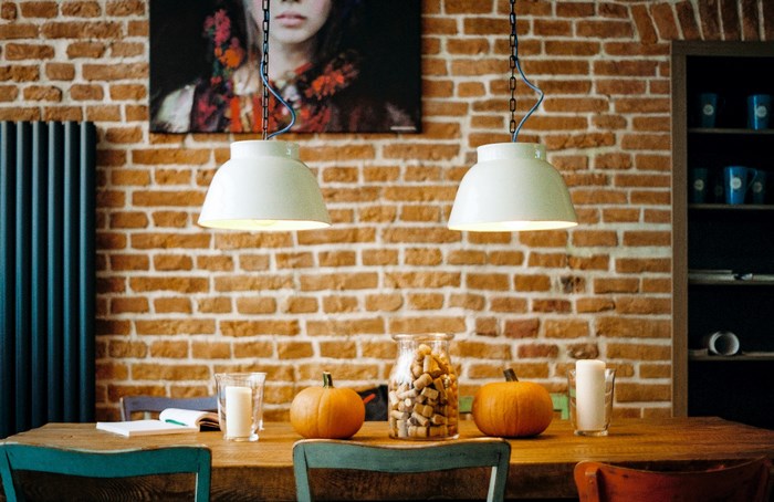 Two pendant lights over a brick wall with pumpkins on a table
