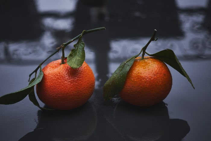 Two tangerines with leaves on a reflective surface