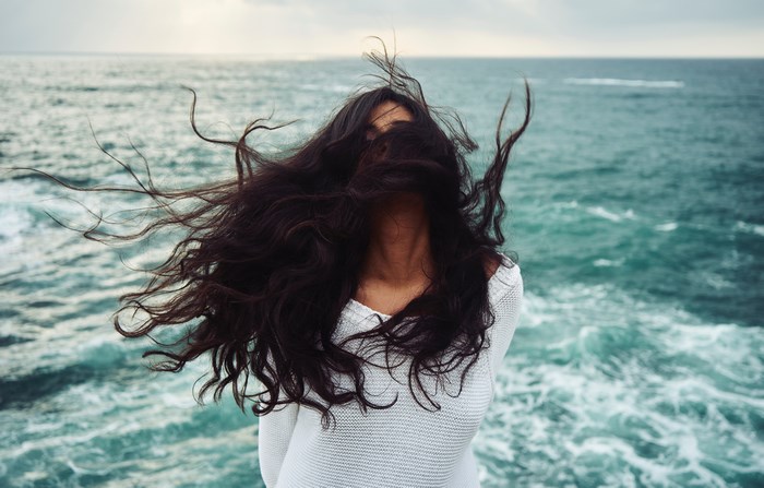 Woman with dark hair blowing in the wind by the sea