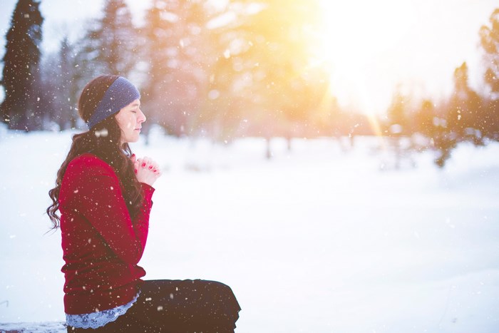 Woman praying in the snow with sun flare
