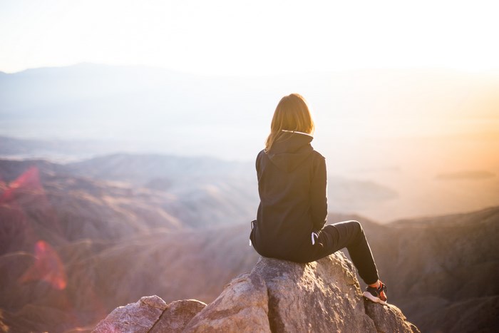 Woman Sitting on Rocky Mountain Peak at Sunrise