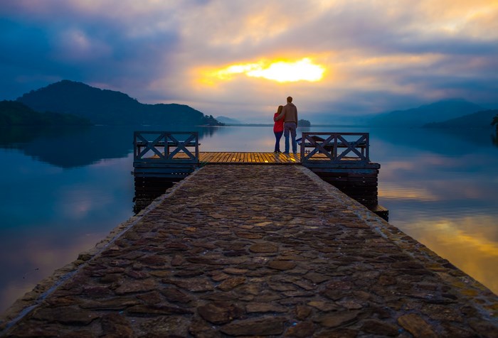 Couple standing on dock by lake at sunrise