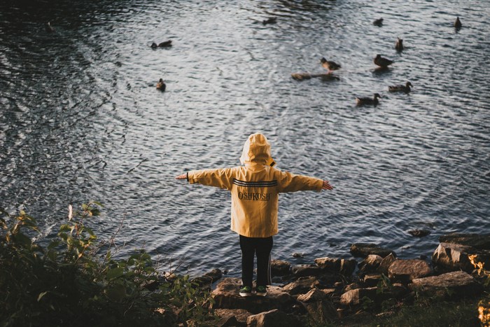 Child in yellow raincoat by a lake with ducks