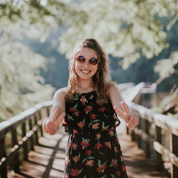 Woman in floral dress and sunglasses making peace signs