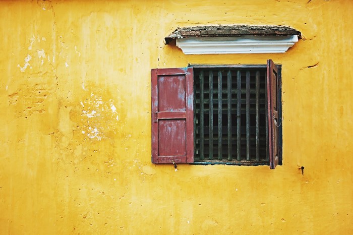 Yellow wall with red shuttered window and bars