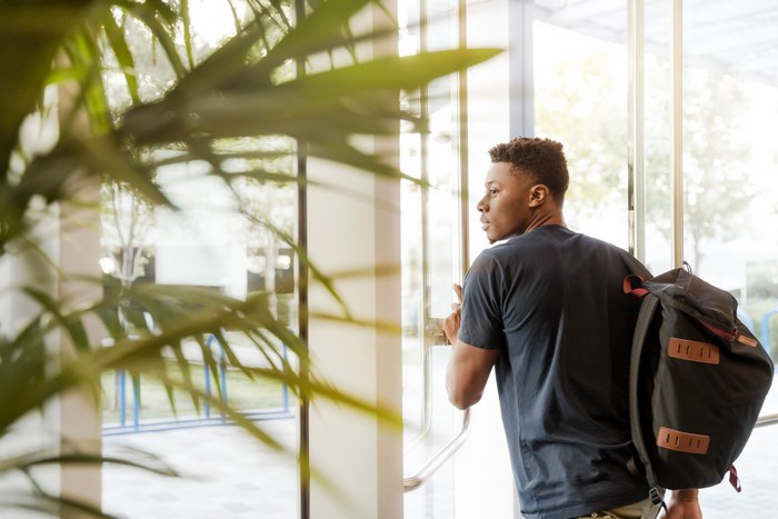 African American man with backpack opening glass door