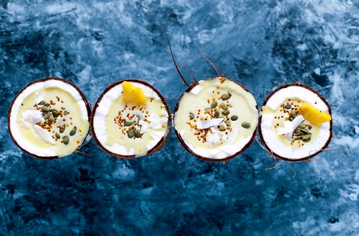 Four coconut halves filled with smoothie and toppings