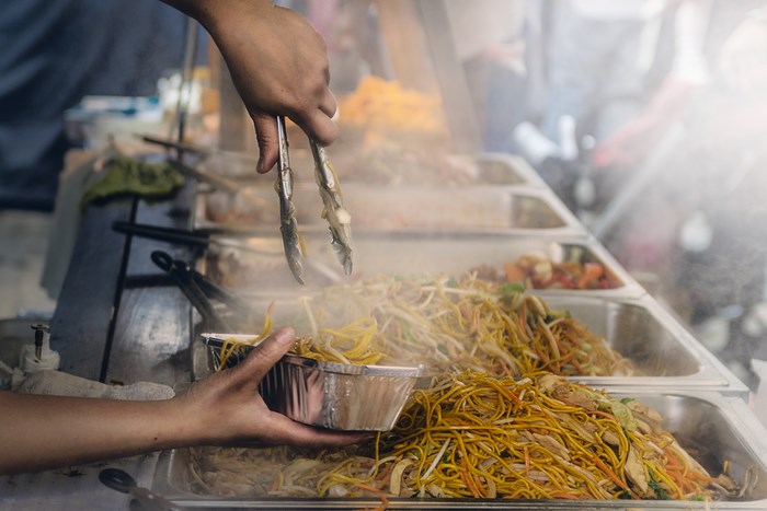 Hand serving noodles with tongs from a food stall