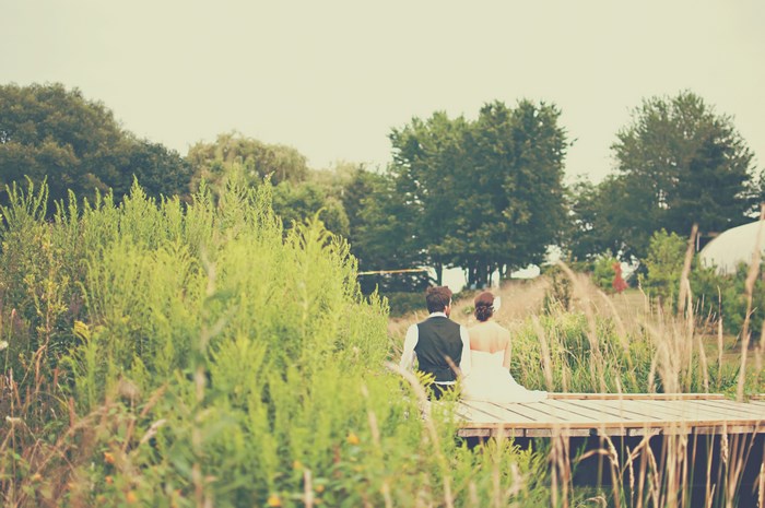 Bride and groom sitting on a wooden jetty in a meadow