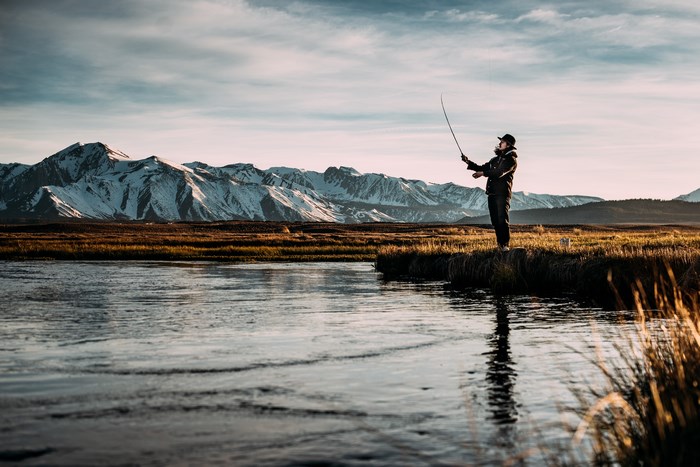 Man fly fishing by snowy mountains at sunset