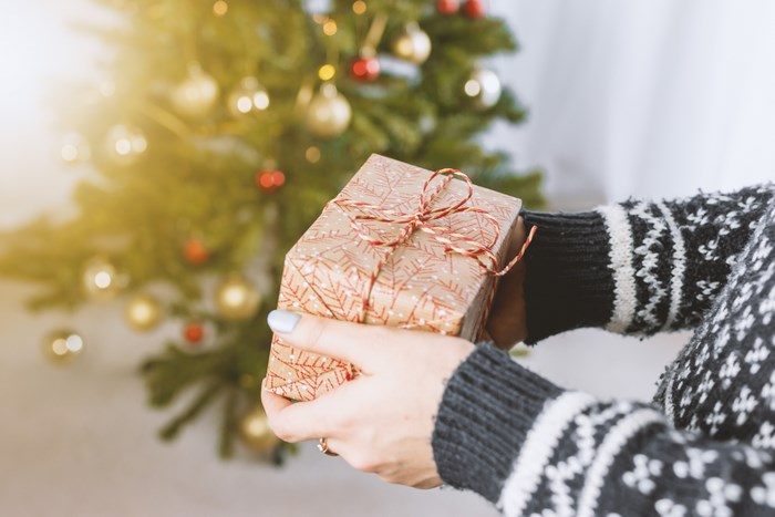 Person holding a Christmas gift near a decorated tree