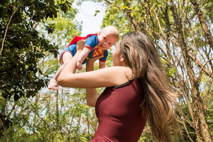 Mother Lifting Baby in Superman Costume Outdoors