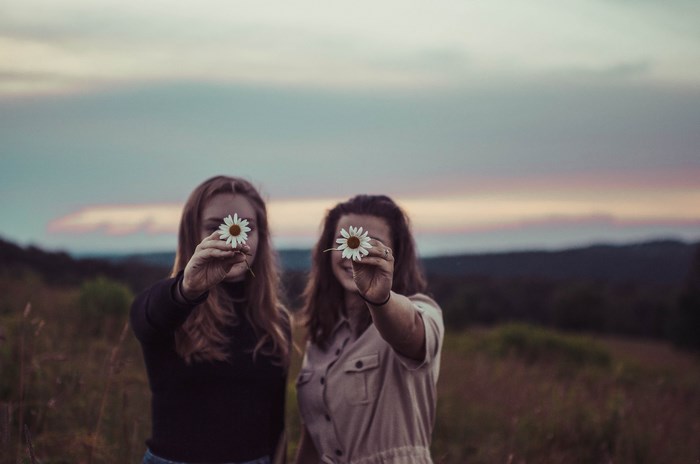 Two women holding daisies in a field at dusk