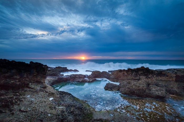 Sunset over the ocean with waves crashing on rocks