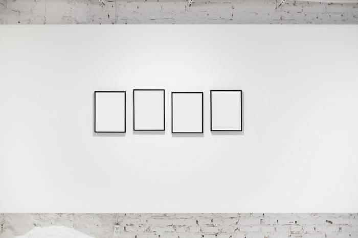 Four empty black frames on a white gallery wall
