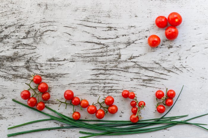 Cherry tomatoes and chives on a wooden surface
