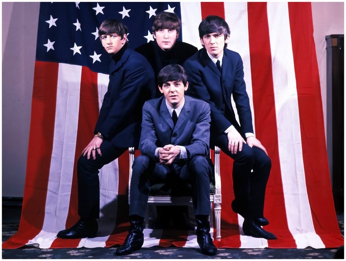 The Beatles posing in front of an American flag