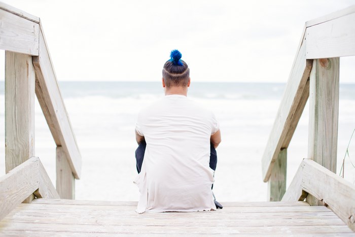 Man with blue hair sitting on wooden stairs at the beach