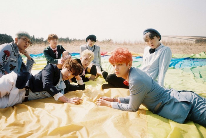 BTS members posing outdoors on a colorful blanket