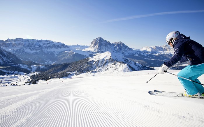 Skier on a groomed slope with snowy mountains