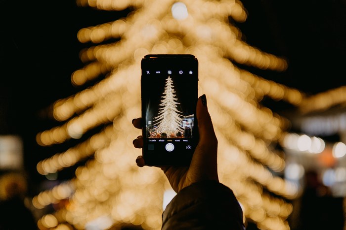 Hand holding iPhone taking picture of Christmas tree lights