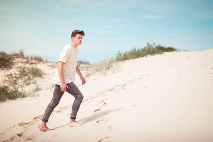 Man climbing sand dune barefoot