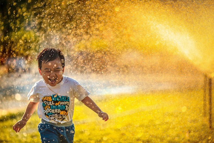 Joyful Child Running Through Water Spray in Golden Light