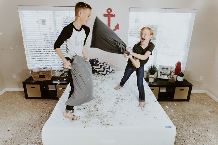 Brother and sister having a pillow fight on a messy bed