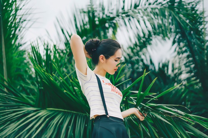 Asian girl in fashion posing among palm leaves