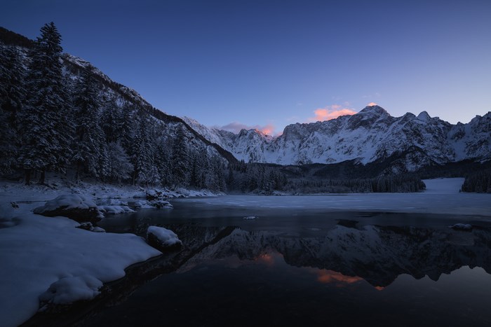 Snowy mountains reflected in a frozen lake at dawn
