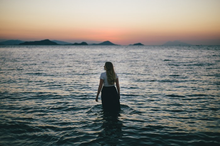 Woman standing in the sea at sunset