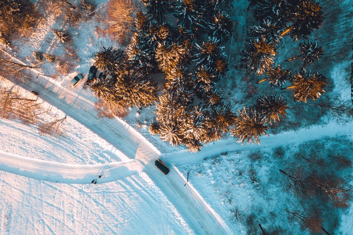 Aerial view of a snowy forest road with cars and people