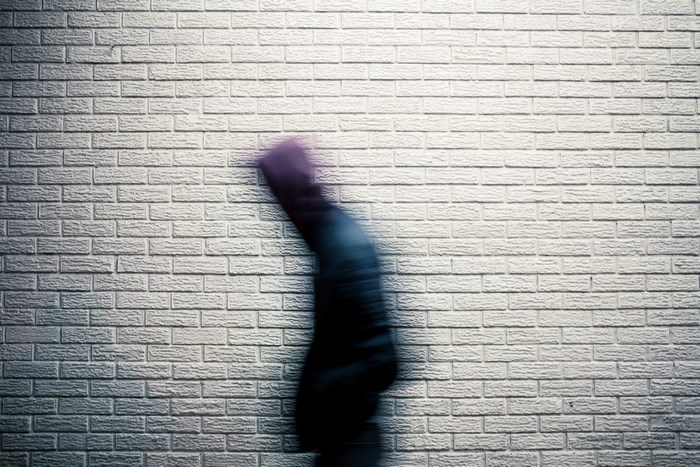 Man walking fast in front of a brick wall