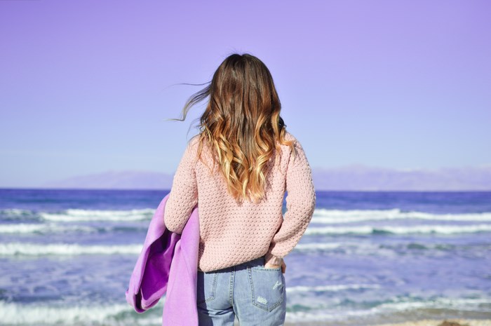 Woman in pink sweater on beach looking at ocean