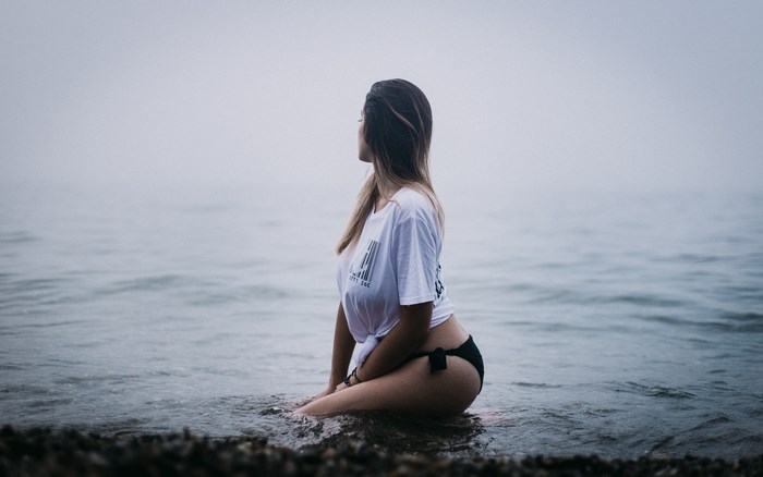 Young Woman Sitting in Calm Water at Beach
