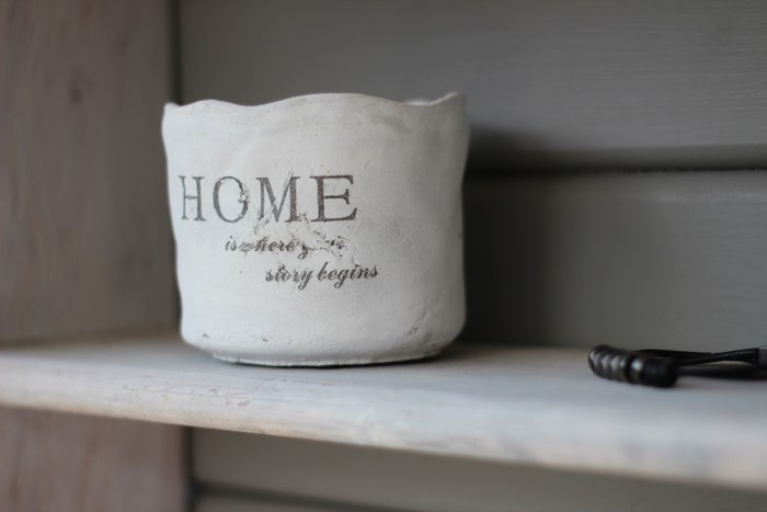 White pot with "HOME is where the story begins" text on a shelf