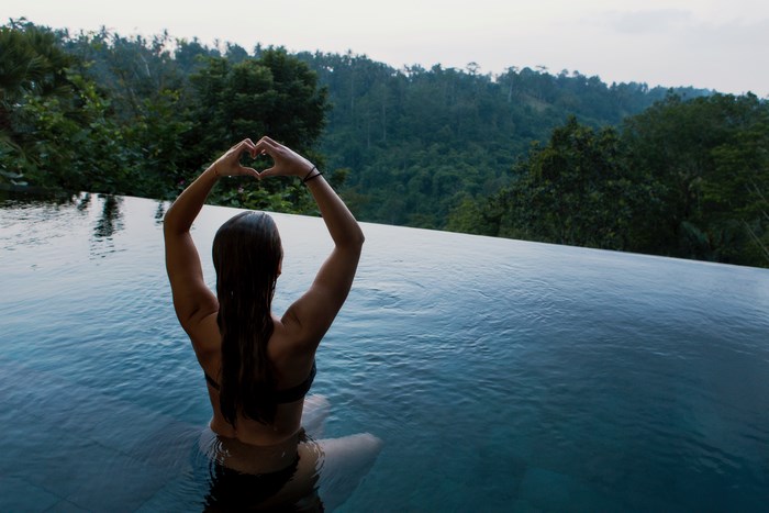 Woman making heart shape in infinity pool overlooking jungle
