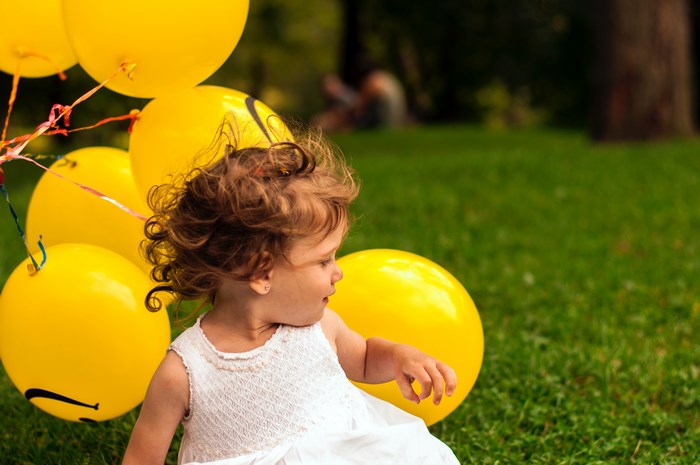 Toddler girl with yellow balloons in a park