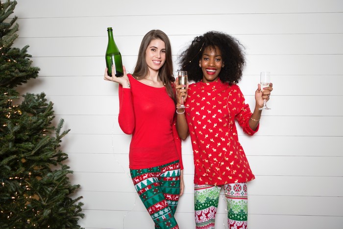 Two women in Christmas pajamas holding champagne