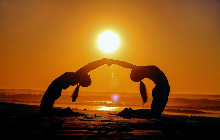 Silhouettes of Two Women Doing Yoga at Beach Sunset